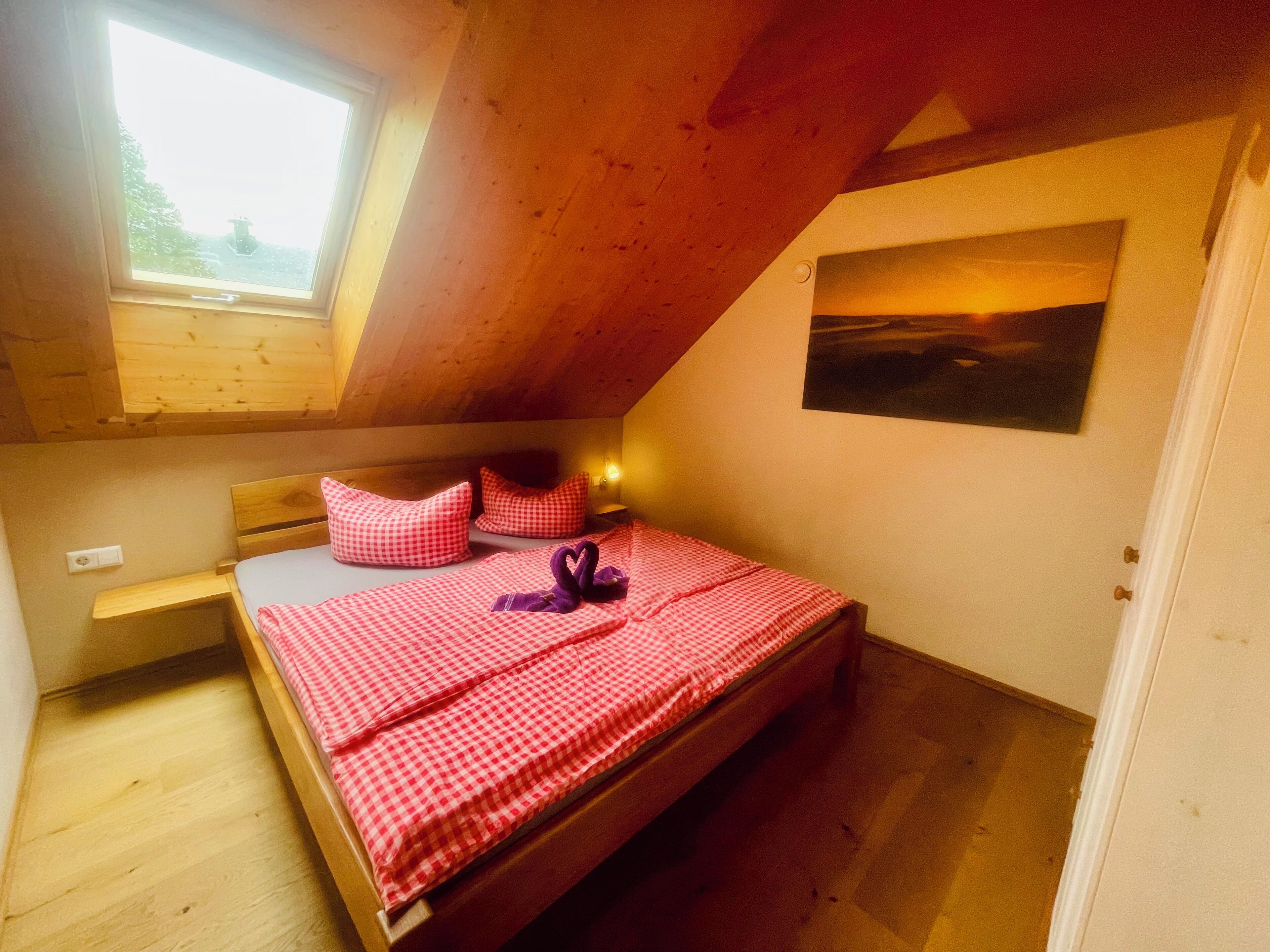 Une petite chambre à coucher accueillante, avec un plafond en pente, un cadre de lit en bois, une literie à carreaux et un tableau accroché au mur.