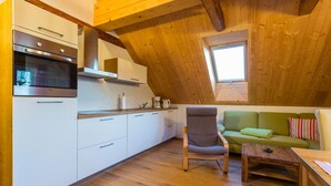 Une cuisine chaleureuse avec des meubles blancs et un four encastré, un plafond en bois, un canapé vert et une petite table.