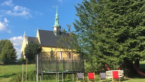 A building with a green spire and a covered outdoor seating area with chairs. - Ferienwohnung Winterstein (Sebnitz)
