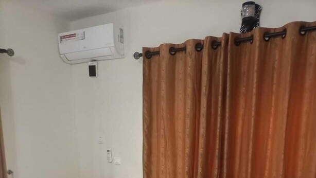Una habitación de hotel con cama, cortinas, aire acondicionado y una mesita de noche con lámpara.