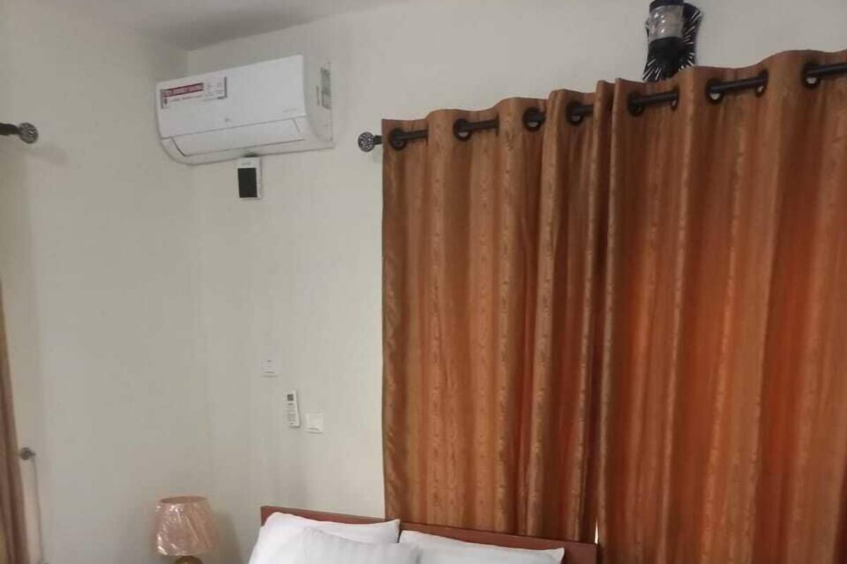 Una habitación de hotel con cama, cortinas, aire acondicionado y una mesita de noche con lámpara.