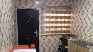 Una cocina compacta con paredes estampadas, un refrigerador, un lavamanos y una ventana con persianas.