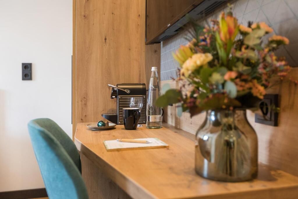 A kitchen counter with a coffee maker, a mug, a glass, and a vase with flowers.