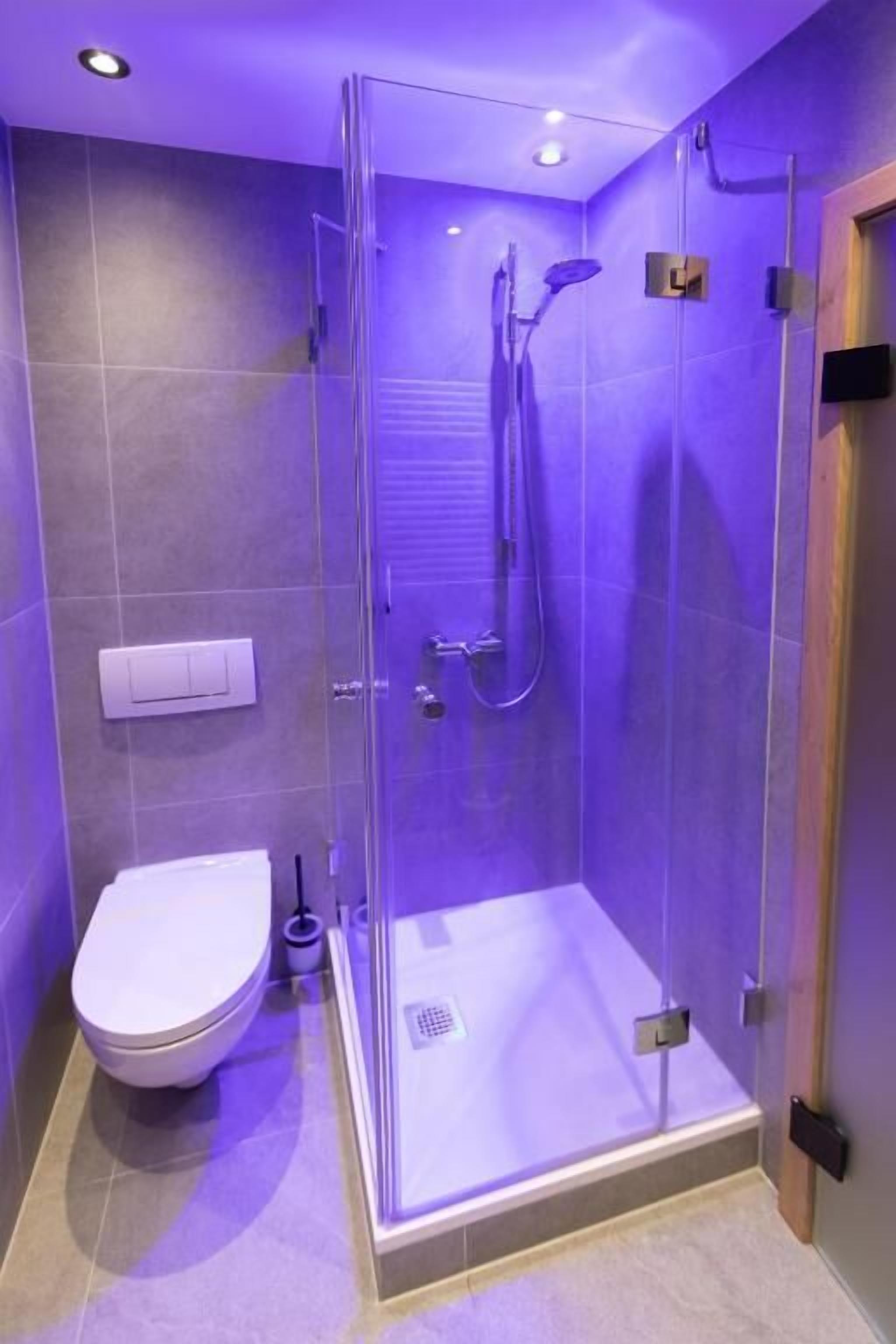 Un baño moderno con ducha de vidrio, inodoro blanco y panel de control a la vista.