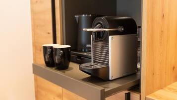A compact kitchenette with a coffee machine, two black mugs, and a wooden cabinet.