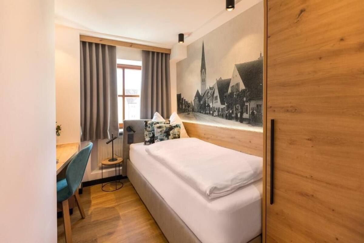 Une chambre d’hôtel avec un lit, un bureau, une chaise, une lampe et une fenêtre avec des rideaux.