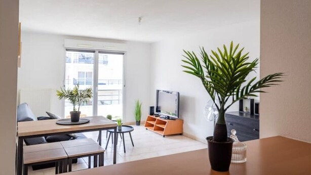 Una sala de estar moderna con comedor, televisor y un amplio ventanal.
