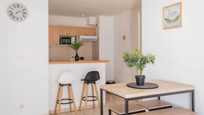Una cocina moderna con armarios de madera, un microondas y una planta en maceta. Hay un comedor con una mesa y dos sillas.