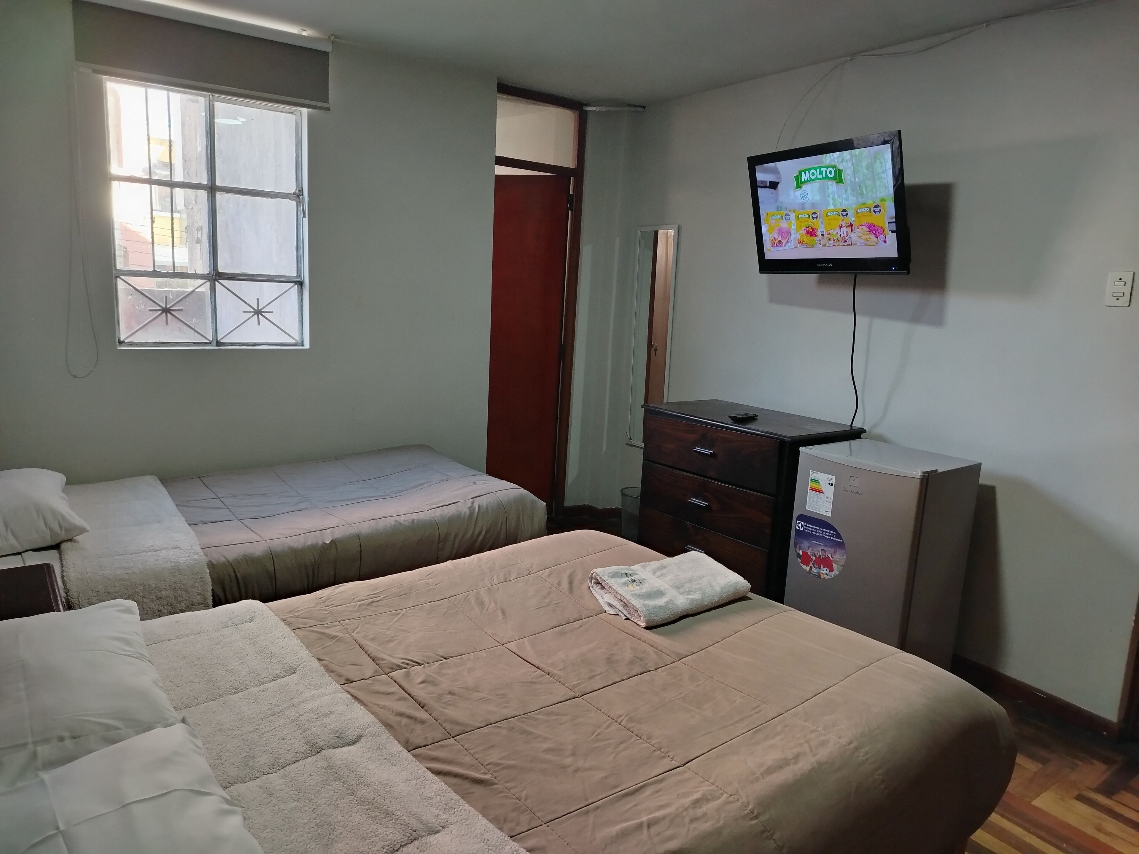 A room with two beds, a television, a dresser, and a window with bars.