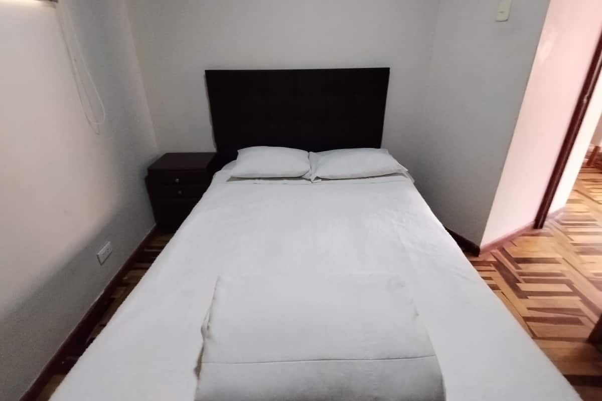 A small, single-bed room with a dark headboard, white bedding, and a wooden floor.