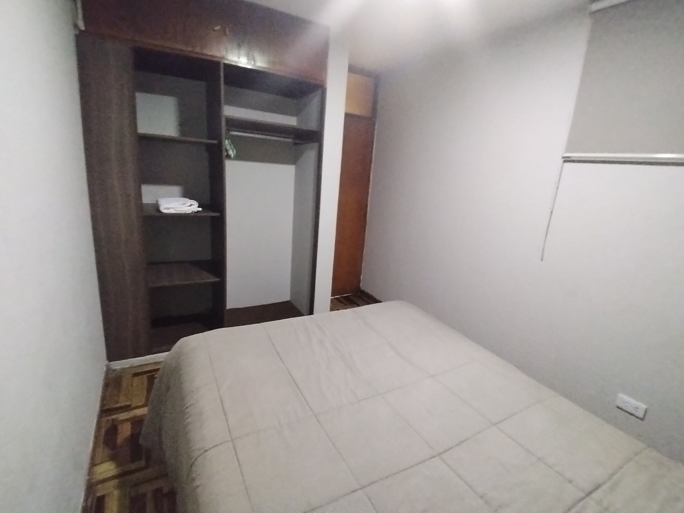 A bedroom with a bed, a wardrobe, and a white wall.
