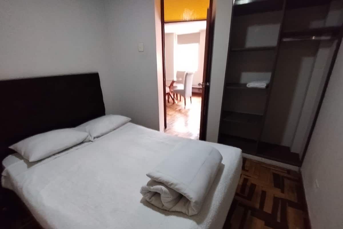 A neatly made bed with white linens in a room with a wooden floor pattern.
