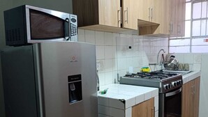 Una cucina compatta con frigorifero, microonde, fornello e mobili in legno.