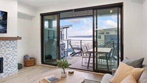 A modern living room with a fireplace, a dining area, and a sliding glass door leading to a balcony with outdoor furniture.