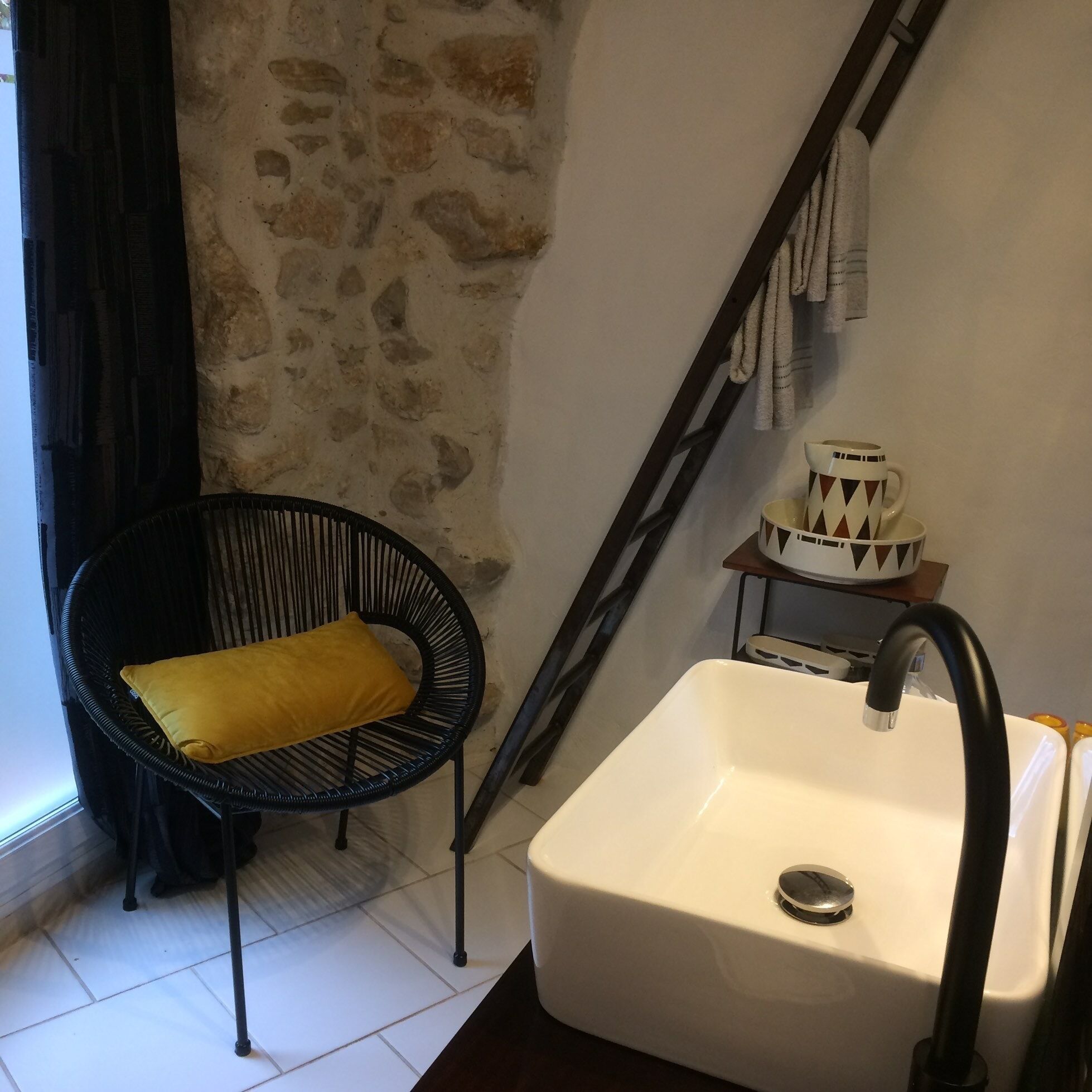 A bathroom with a white sink, black faucet, and a chair with a yellow cushion.