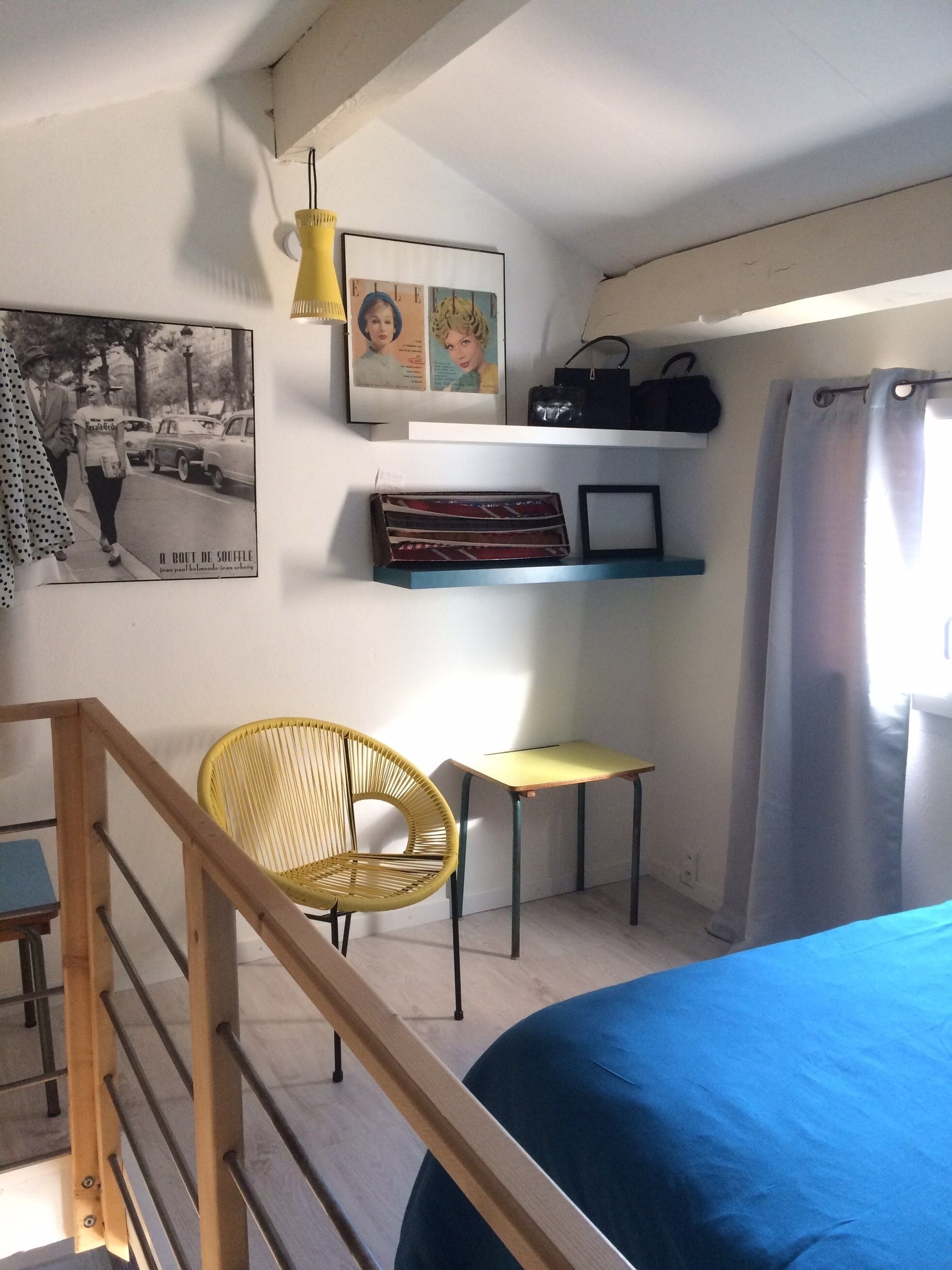 Een slaapkamer met een bed, een stoel, een klein tafeltje, een plank met spullen en een foto aan de muur.
