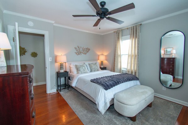 A bedroom with a bed, bedside lamps, a ceiling fan, a dresser, and a large mirror.