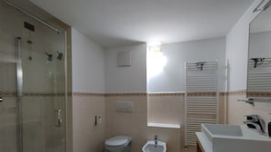 Et badeværelse med brusekabine i glas, toilet, bidet og håndvask.