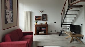 En stue med en rød sofa, et træ TV-skab, en trappe og en reol.