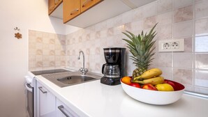 A kitchen with a white countertop, a coffee maker, a fruit bowl, and a sink. - Apartments Adria (Rovinj)