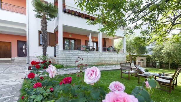 A two-story house with a balcony, a stone wall, and a garden with roses. - Apartments Adria (Rovinj)