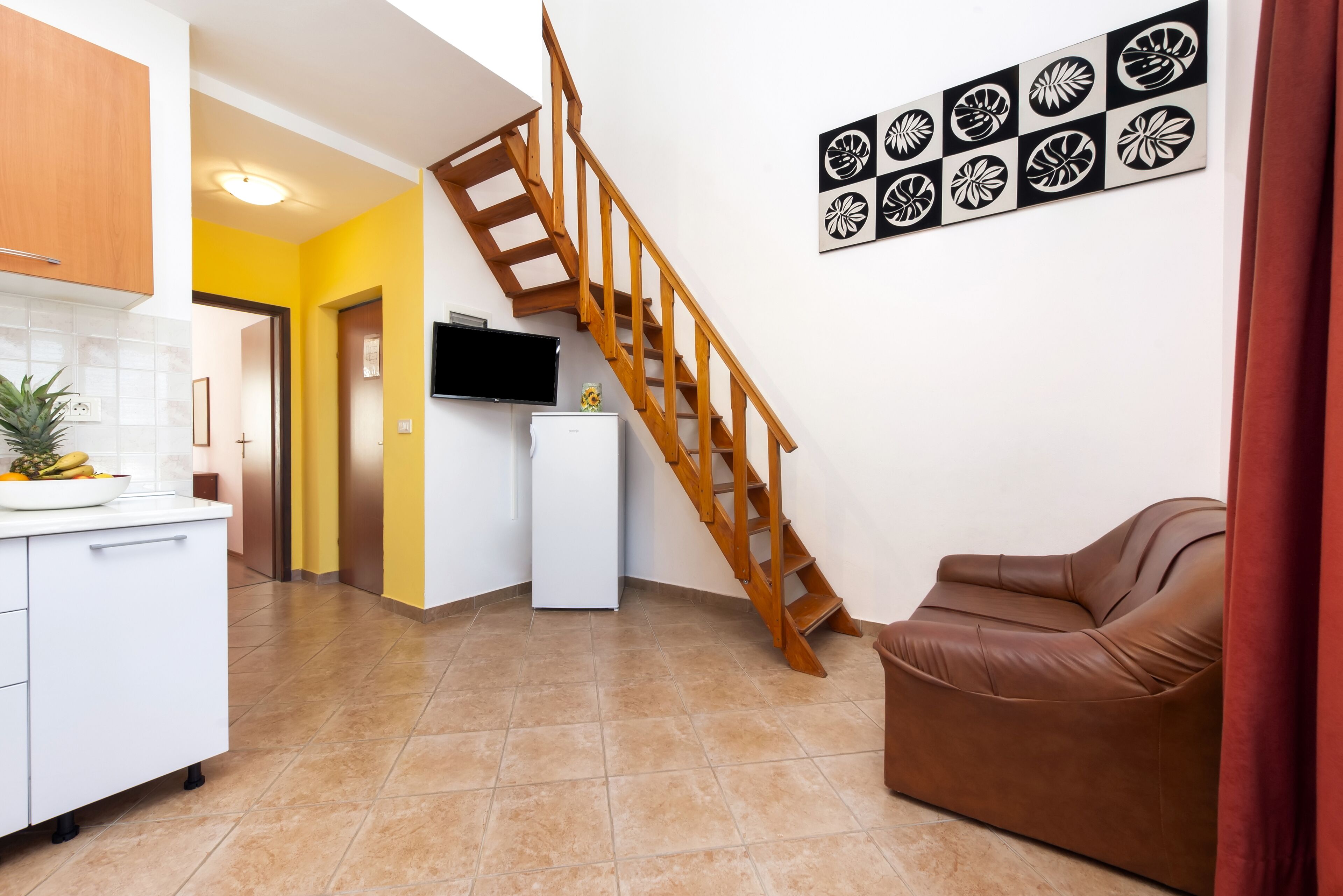 A modern kitchen with a wooden staircase, a white refrigerator, and a brown leather couch.