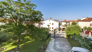 A courtyard with a white building, a stone pathway, and a parked car. - Apartments Adria (Rovinj)