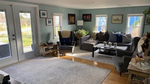 A living room with a sofa, armchairs, a coffee table, and a rug. There are framed pictures on the wall and a plant on a side table. - Relax on the South Shore, steps from 2 beaches, ocean views & hot tub. (East River Point)