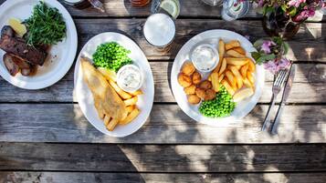A wooden table with two plates of food, a glass of beer, and a vase with flowers.
