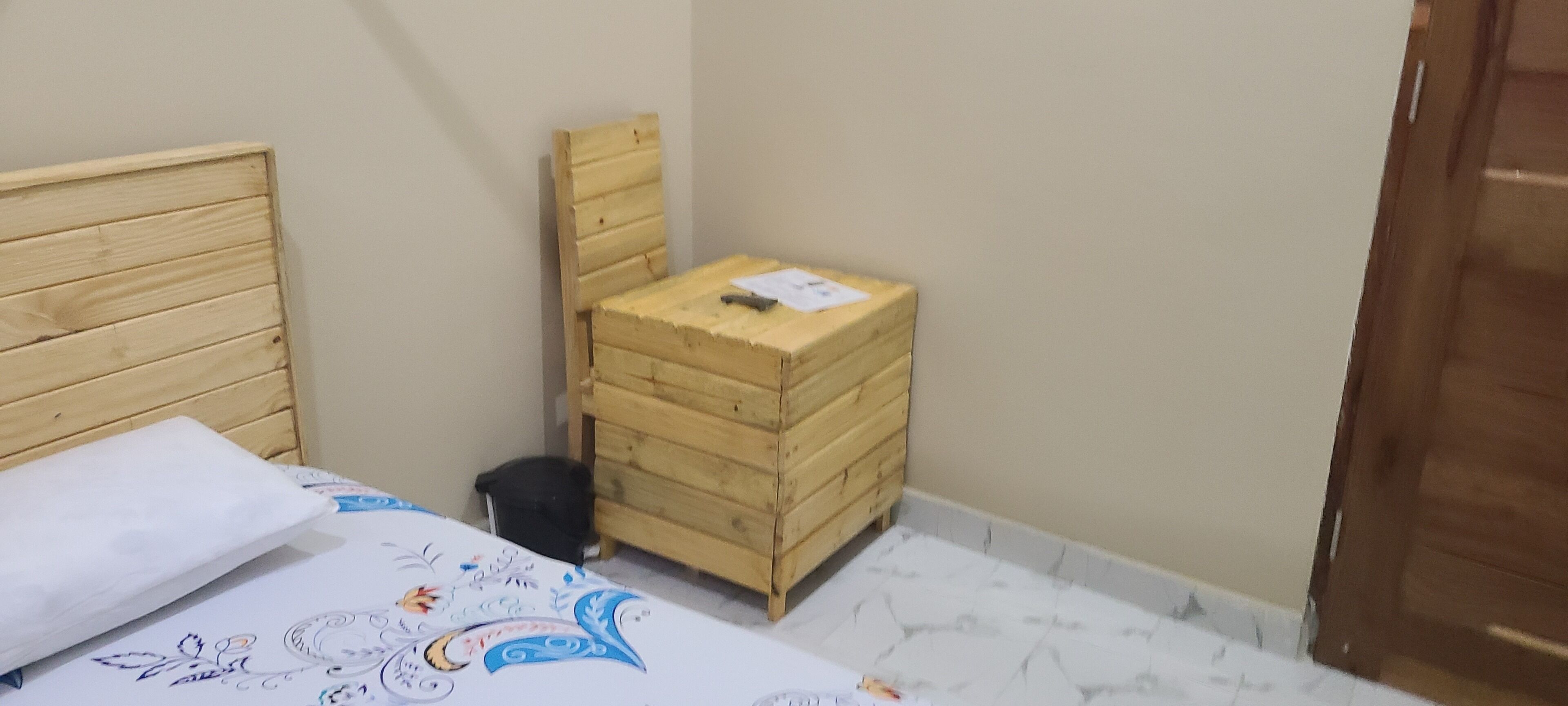 A small room with a wooden bed, a wooden chest of drawers, and a tiled floor.