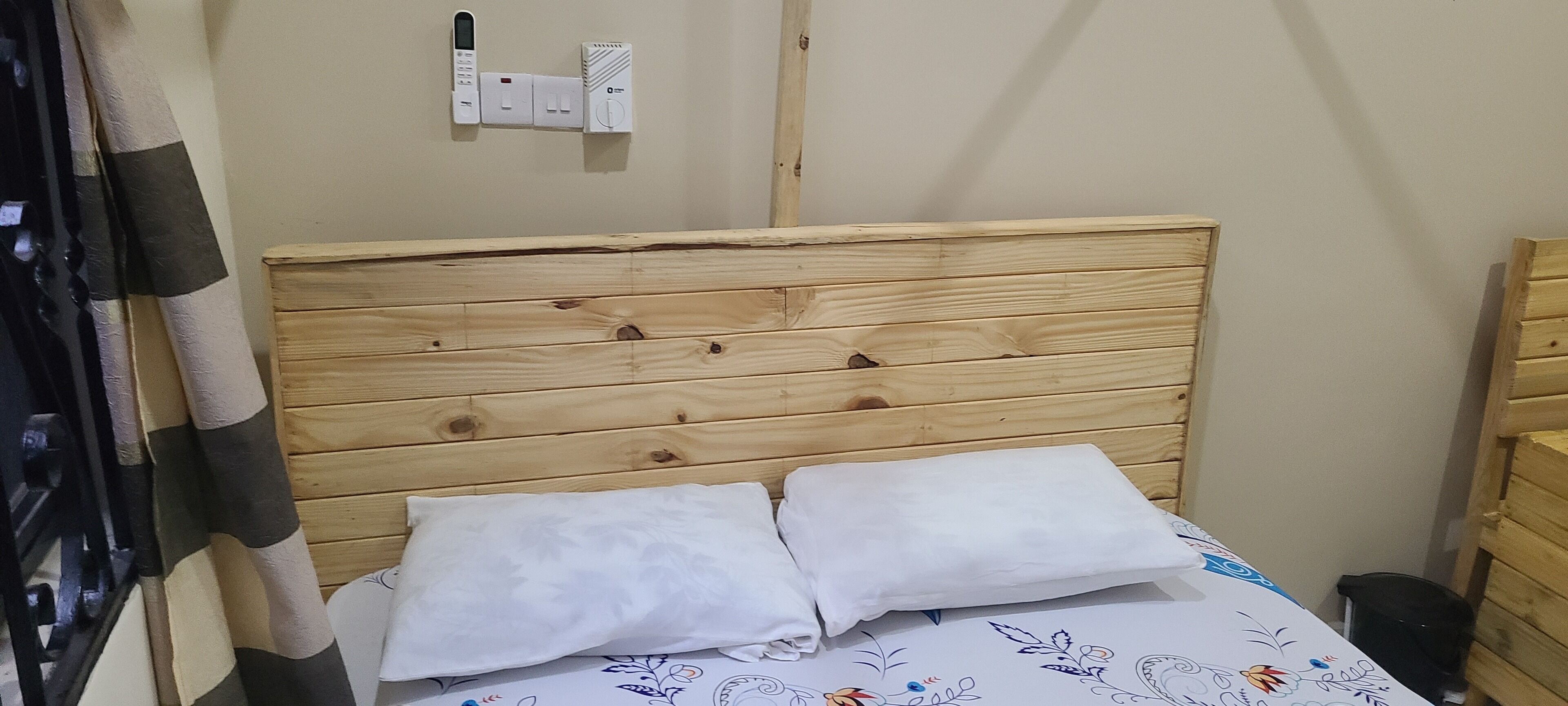 A wooden headboard bed with two pillows, a power outlet, and a thermostat on the wall.