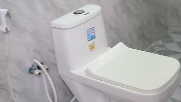 Uma casa de banho com sanita branca, secador de mãos e dispensador de sabonete fixado na parede.