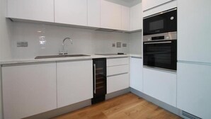Une cuisine moderne avec des armoires blanches, un évier en acier inoxydable et des appareils électroménagers intégrés, notamment un four à micro-ondes et un four traditionnel.
