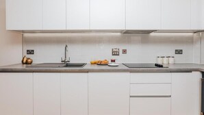 Une cuisine moderne avec des meubles blancs, un évier en acier inoxydable et un plan de travail sur lequel on trouve un grille-pain et des bocaux.