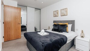 Une chambre moderne avec un grand lit, une porte en bois et une table de chevet blanche.