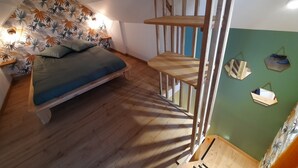 A bedroom with a bed, wooden floor, a slanted ceiling, and a green wall with decorative items. - Gîte La Ruchette (Sainte-Marguerite-sur-Duclair)