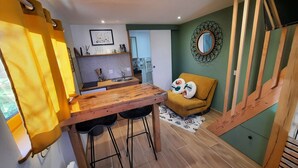 A compact kitchen with a wooden table and stools, a sofa with cushions, and a decorative mirror on the wall. - Gîte La Ruchette (Sainte-Marguerite-sur-Duclair)