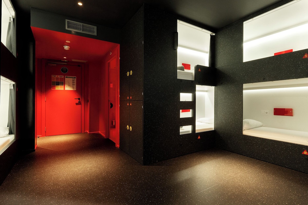Un pasillo que lleva a una habitación con literas, una puerta roja y un respiradero en el techo.