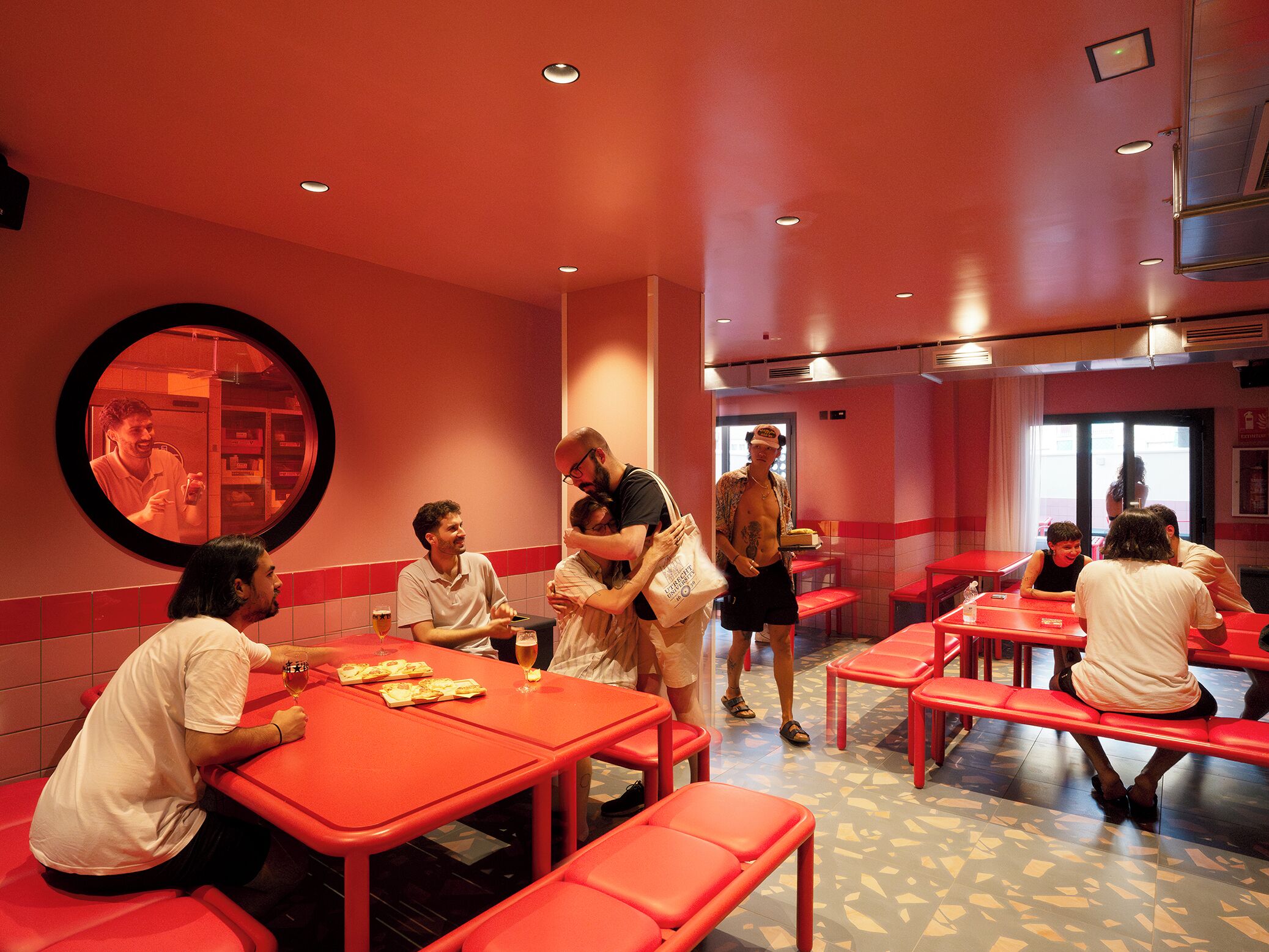 A restaurant with red tables and benches, a round mirror on the wall, and a tiled floor.