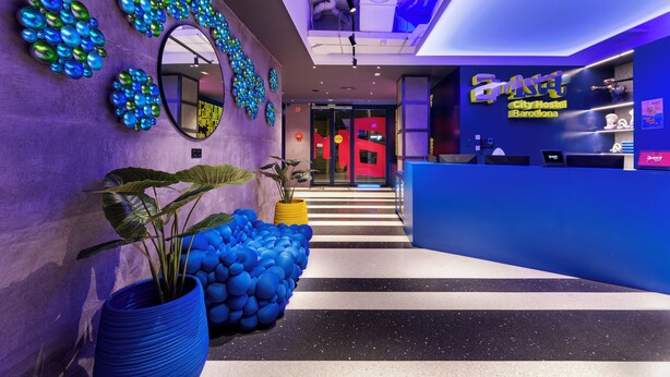 Eine moderne Hotelhalle mit einer Rezeption, einem großen Spiegel und dekorativen, blauen und grünen Kugeln an den Wänden.
