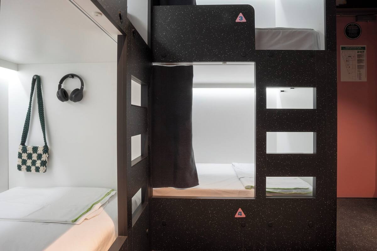 Habitación con literas, un colchón blanco, auriculares y un bolso de ganchillo.
