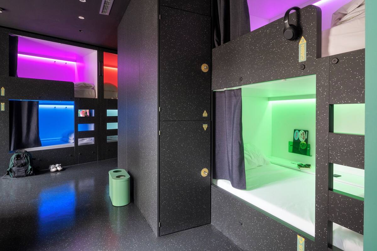 Una habitación moderna y compacta con literas, un cubo de basura pequeño y una puerta con cerradura.