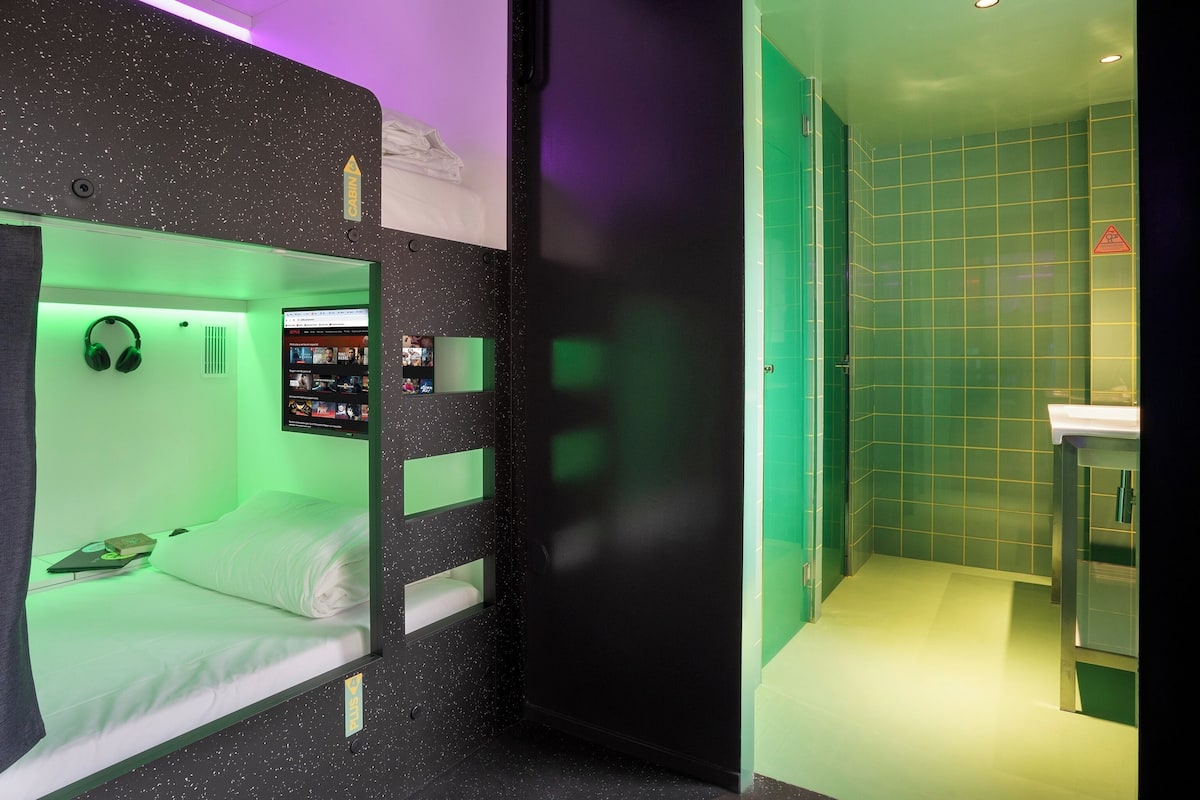 Una habitación con literas, un escritorio pequeño con una computadora y una pared iluminada de verde.