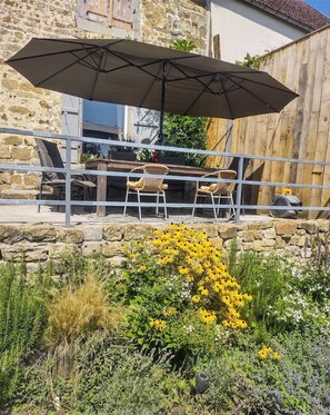 An outdoor patio with a table and chairs, a large umbrella, and a stone wall backdrop. - Boerderij , 8 Persoons met Zwembad en Groots Uitzicht (Laferté-sur-Amance)