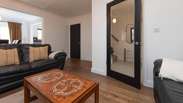 Una sala de estar moderna con un sofá de cuero negro, una mesa de centro de madera y una puerta negra que da a una escalera.