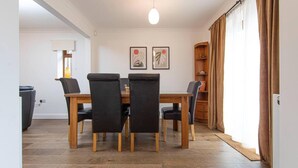 Un comedor con una mesa de madera y sillas negras, dos obras de arte enmarcadas en la pared y un aparador de madera con estantes.