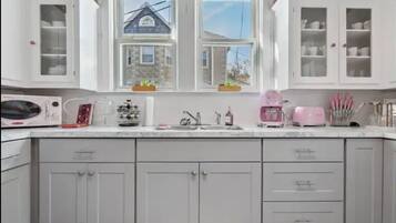 A kitchen with white cabinets, a window with a view of a house, and various kitchen appliances.