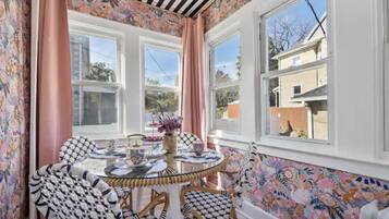 A dining area with a round glass table, patterned chairs, and a view of the outside through large windows.