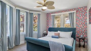 A bedroom with a large bed, a ceiling fan, and patterned wallpaper.