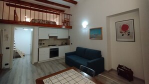 Um espaço de estar compacto com cozinha compacta, um sofá azul, uma mesa de jantar e uma escada que leva a um andar superior.